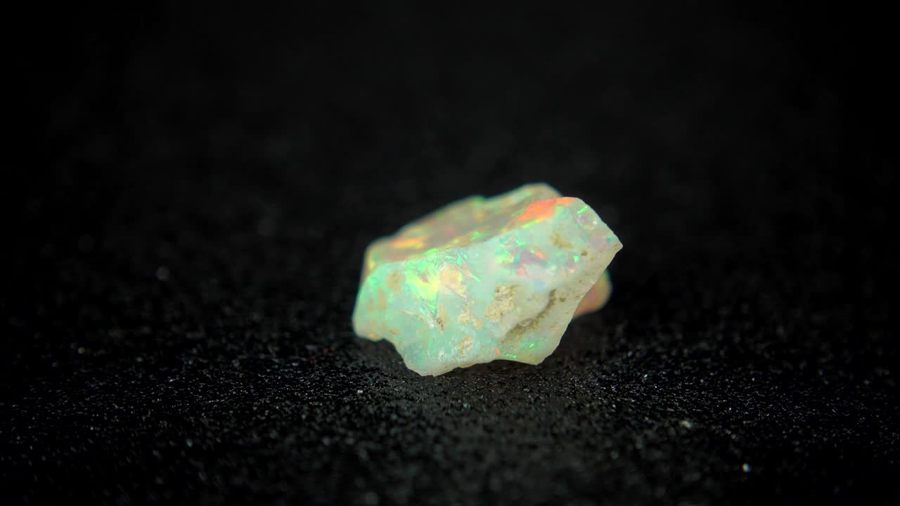 girando sin problemas un mineral de colores (opal) frente al fondo negro