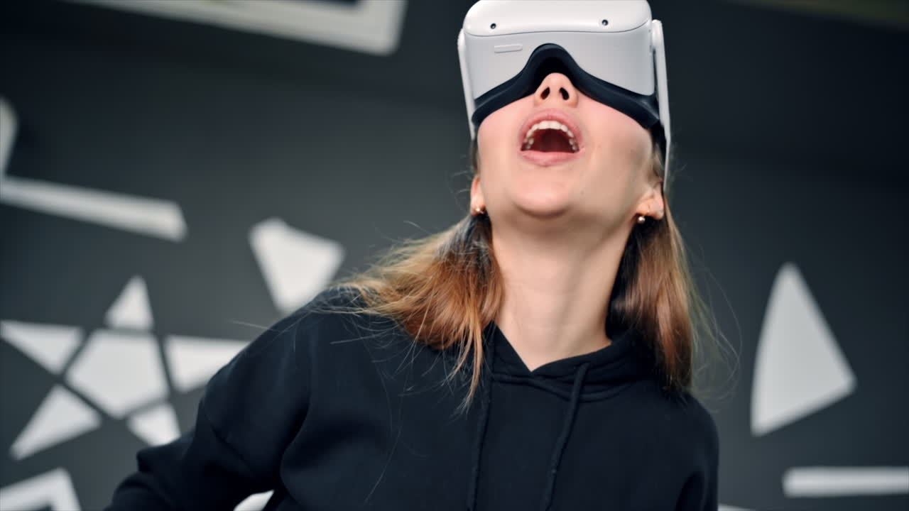 A young woman in VR glasses with controllers is excited while playing VR games. Slow motion