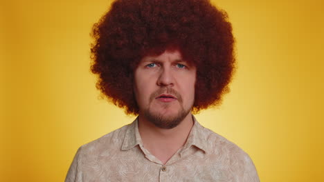 confused man with afro wig shrugs and looks at camera