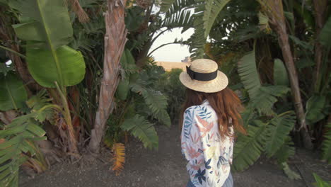 woman in straw hat walking through palm trees