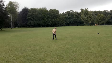 Elderly-man-walking-alone-through-park-field,-aerial-arc-shot