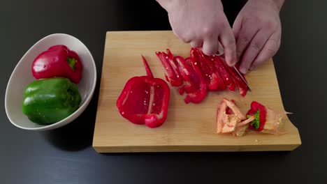 Manos-Masculinas-Rebanando-Pimiento-Rojo-Y-Verde-En-Una-Tabla-De-Cortar-De-Madera---Disparo-En-ángulo-Alto,-Primer-Plano