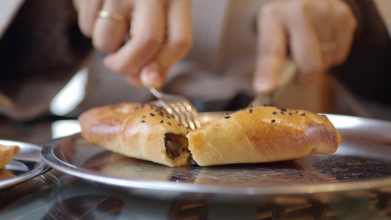 Close-Up of Hands Cutting a Savory Baked Pastry with Fork and Knife