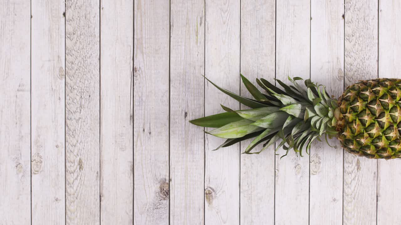 Pineapple rolling in place on right side of  wooden theme. Stop motion