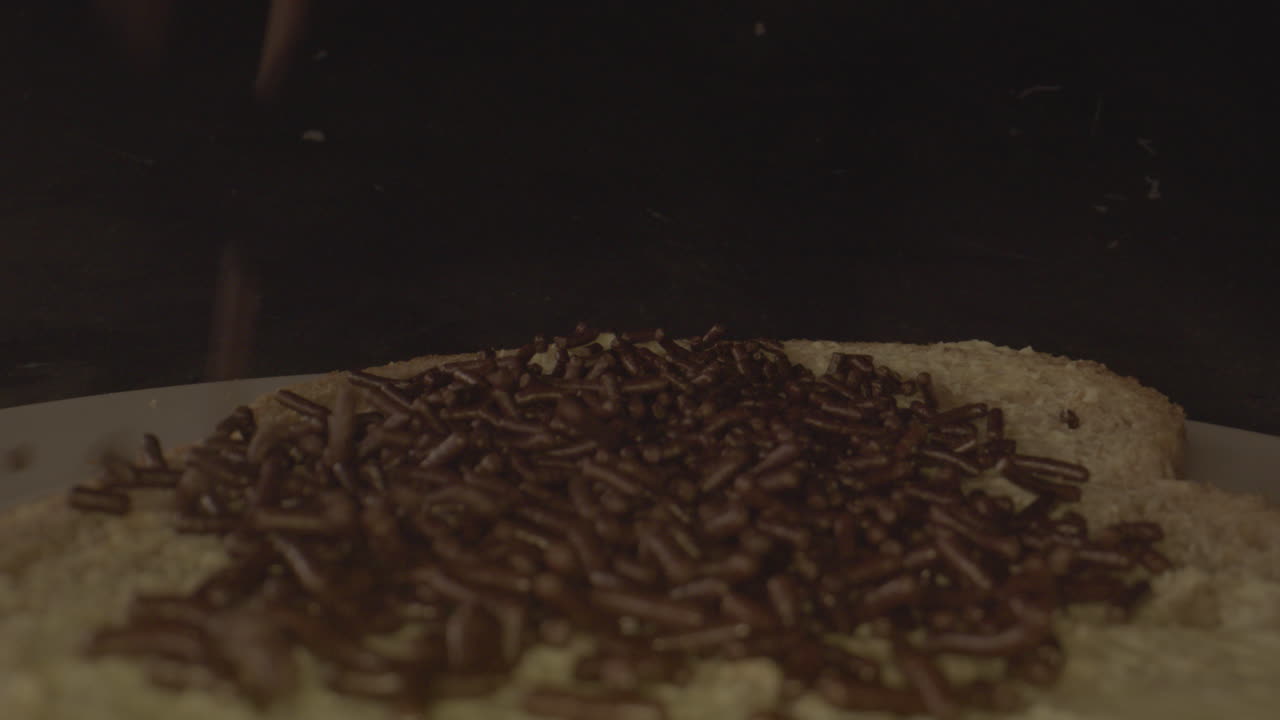 tiro macro de chispas de chocolate cayendo sobre una rebanada de pan con mantequilla