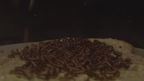 tiro macro de chispas de chocolate cayendo sobre una rebanada de pan con mantequilla