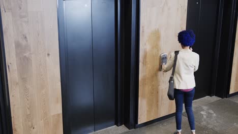 Biracial-businesswoman-with-blue-afro-talking-on-smartphone-and-using-elevator,-slow-motion
