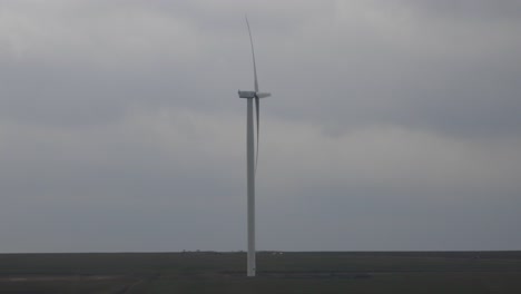 side view of wind turbine on field with cloudy sky in background. full shot