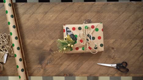 a young woman wraps a holiday christmas present on a wooden table in polka dot wrapping paper a card and a mistletoe ready to put under the xmas tree