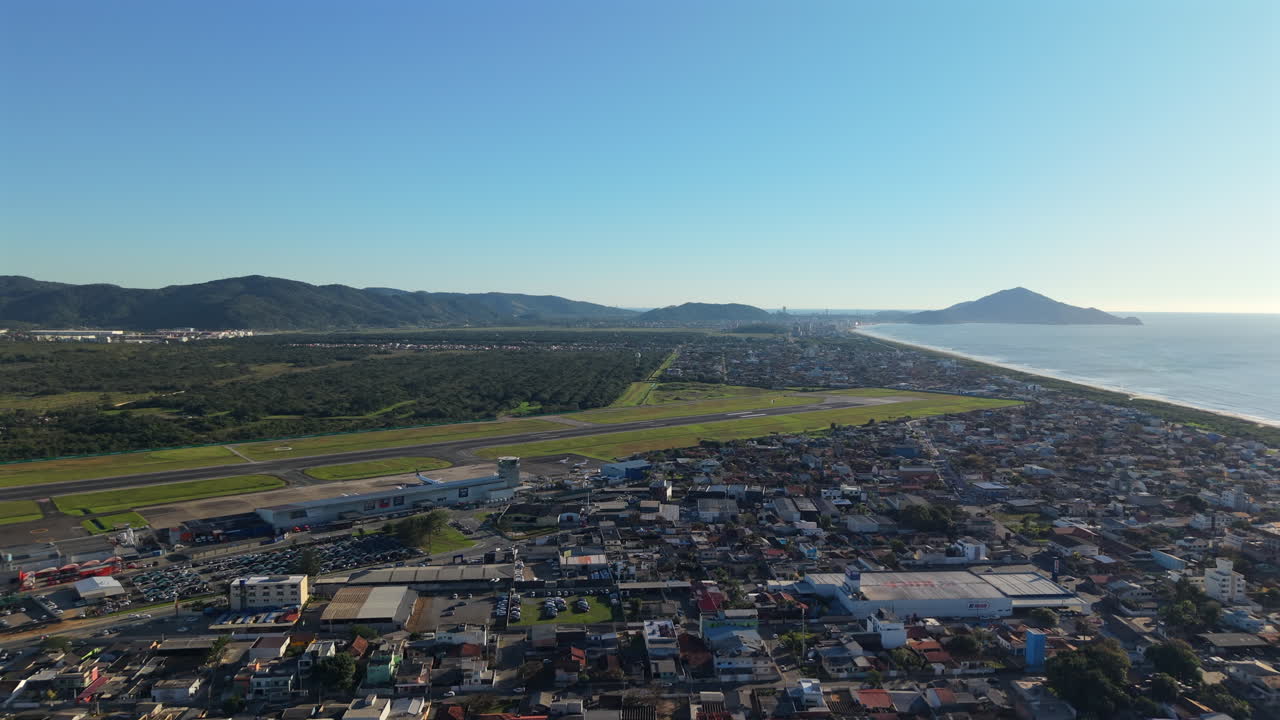 Aerial view of coastal Navegantes International Airport with distant hills and ocean under clear blue sky, Navegantes, Santa Catarina, Brazil