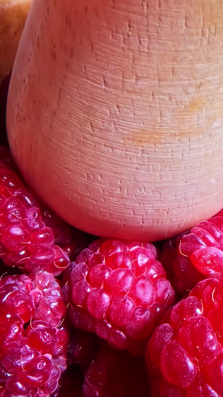 Lamponi succosi vengono schiacciati in una ciotola di legno, rilasciando succo rosso vibrante