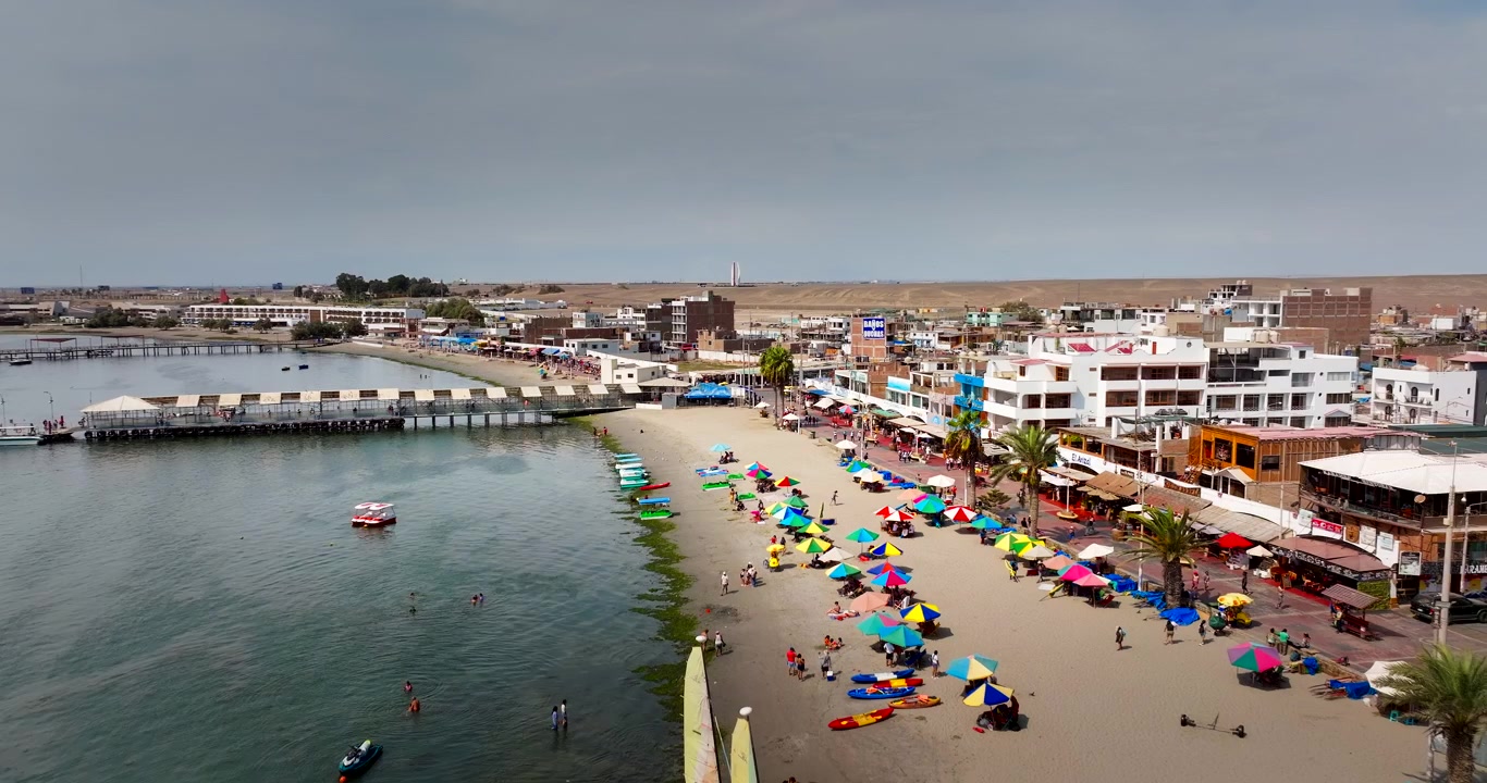 Chapéus de sol coloridos e banhistas na praia de Paracas, no Peru. Sobrevoo aéreo.