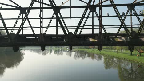 The-camera-slowly-rises-above-the-river-and-reveals-a-rusty-bridge-structure-from-which-pigeons-fly-away