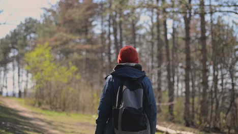 een onherkenbare jonge vrouw met een rode wollen muts loopt door het bos en kijkt van links naar rechts