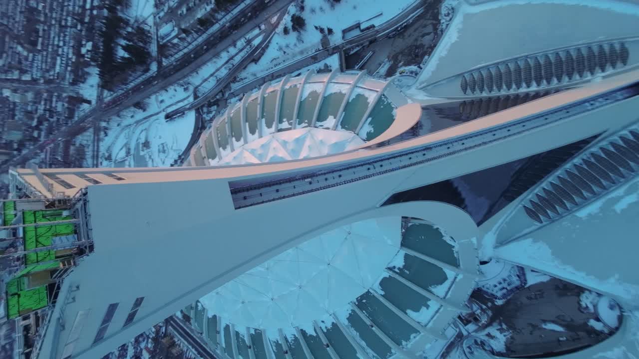 Drone flies over snowy Montreal Olympic Stadium in winter, sunset glow highlights architecture