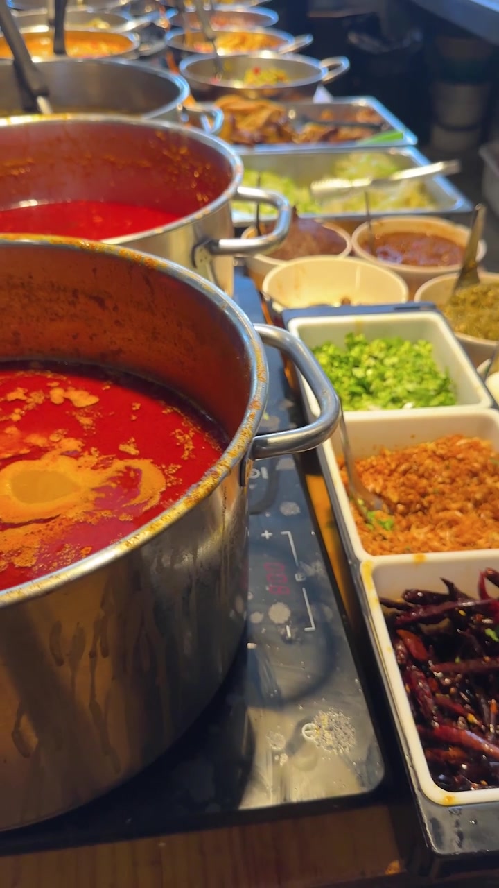 Primo piano con zoom indietro di zuppa di curry piccante rosso vivace in grandi pentole a un buffet thailandese.