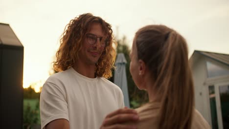 A-curly-haired-guy-in-glasses-fixes-his-girlfriend's-hair-and-hugs-her.-Rest-in-the-country-house