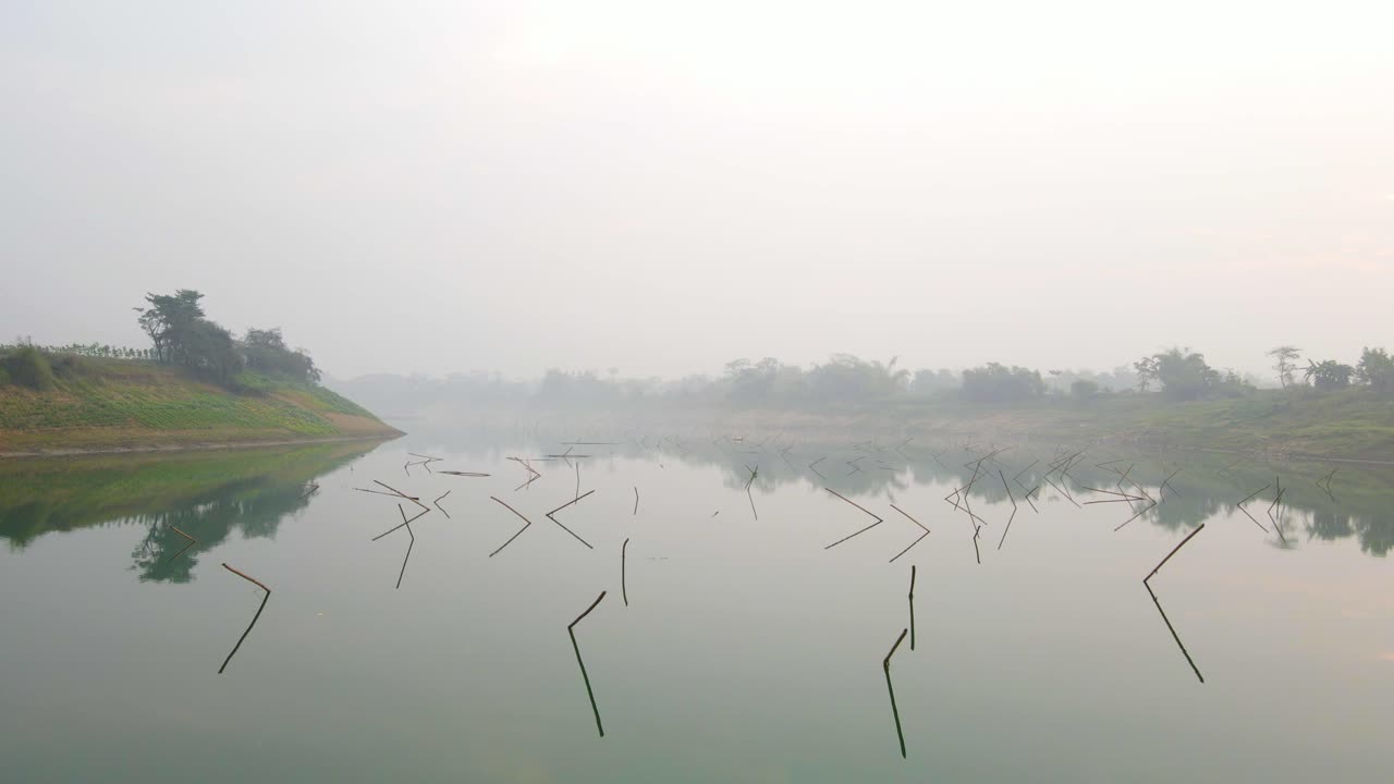 las imágenes aéreas capturan una mañana nublada, volando bajo sobre un gran río tranquilo y reflectante, con palos que sobresalen del agua.