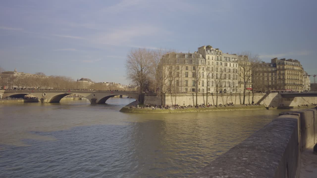 Seine River in Paris, historic stone bridge, people enjoying sunny winter day long shore. Panning