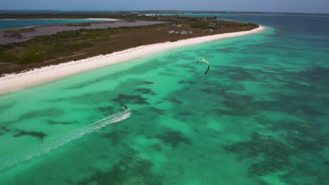 A-kitesurfer-navigating-turquoise-waters-along-a-pristine,-isolated-beach,-aerial-view