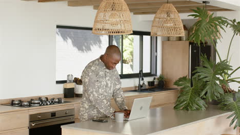 military man using laptop and smartphone in modern kitchen, working remotely