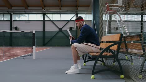 hombre sentado en un banco en una cancha de tenis cubierta