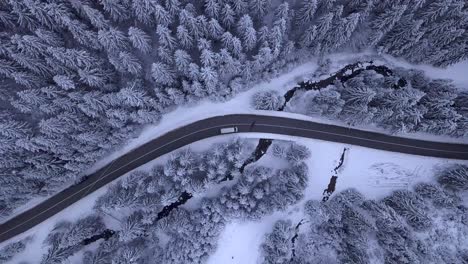 Luftaufnahmen-Eines-Autos,-Das-Auf-Einer-Straße-Vorbeifährt,-Die-Den-Schneebedeckten-Wald-Trennt