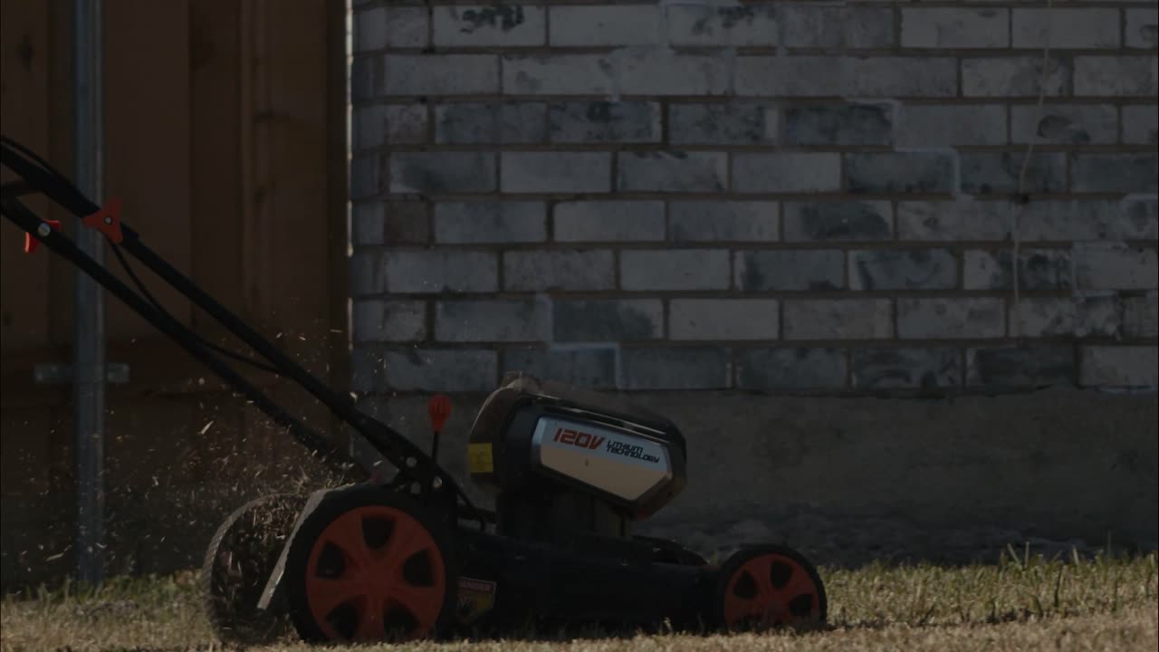 리튬 배터리로 작동되는 잔디 깎는 기계가 뒤뜰의 잔디 위로 밀리고 있습니다.