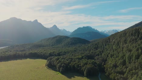 reverse aerial drone view of tree covered landscape of rugged, wild and remote southern alps mountain ranges in glenorchy, new zealand aotearoa