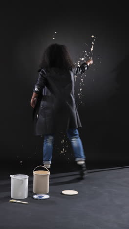 vertical video: artist creating abstract splatter art on black wall in grunge studio
