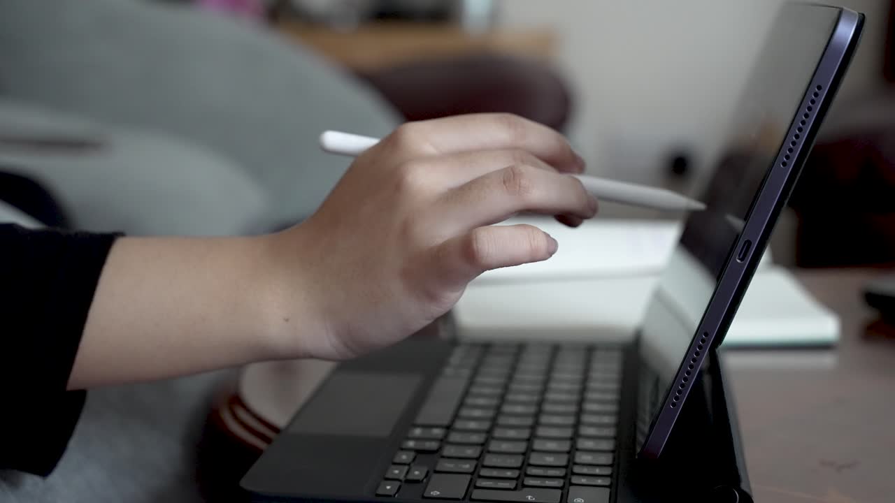 una persona utiliza un bolígrafo en una tableta ipad mientras trabaja en un entorno doméstico, destacando la versatilidad de las herramientas digitales para la productividad y la creatividad en el hogar