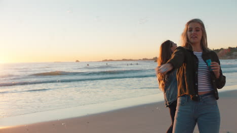 Freundinnen-Blasen-Am-Strand-Bei-Sonnenuntergang-Seifenblasen-Und-Haben-Spaß-Im-Sommer,-Spielen-Am-Meer-Und-Genießen-Die-Freundschaft
