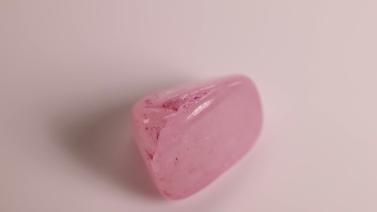 A rose quartz stone spins smoothly on a white surface, showcasing its polished texture and soft pink hue