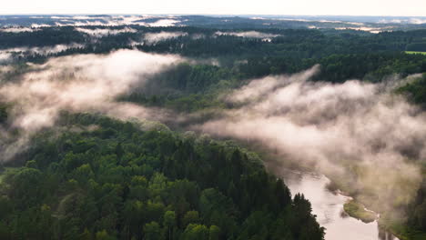 sweeping views of the gauja river from a castle tower overlooking gauja national park in sigulda, latvia; slow aerial rotation over low lying clouds blanketing verdant valley.