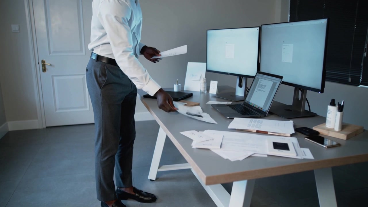 Picking up papers, man in white shirt scanning at desk with laptop preparing report, copy space
