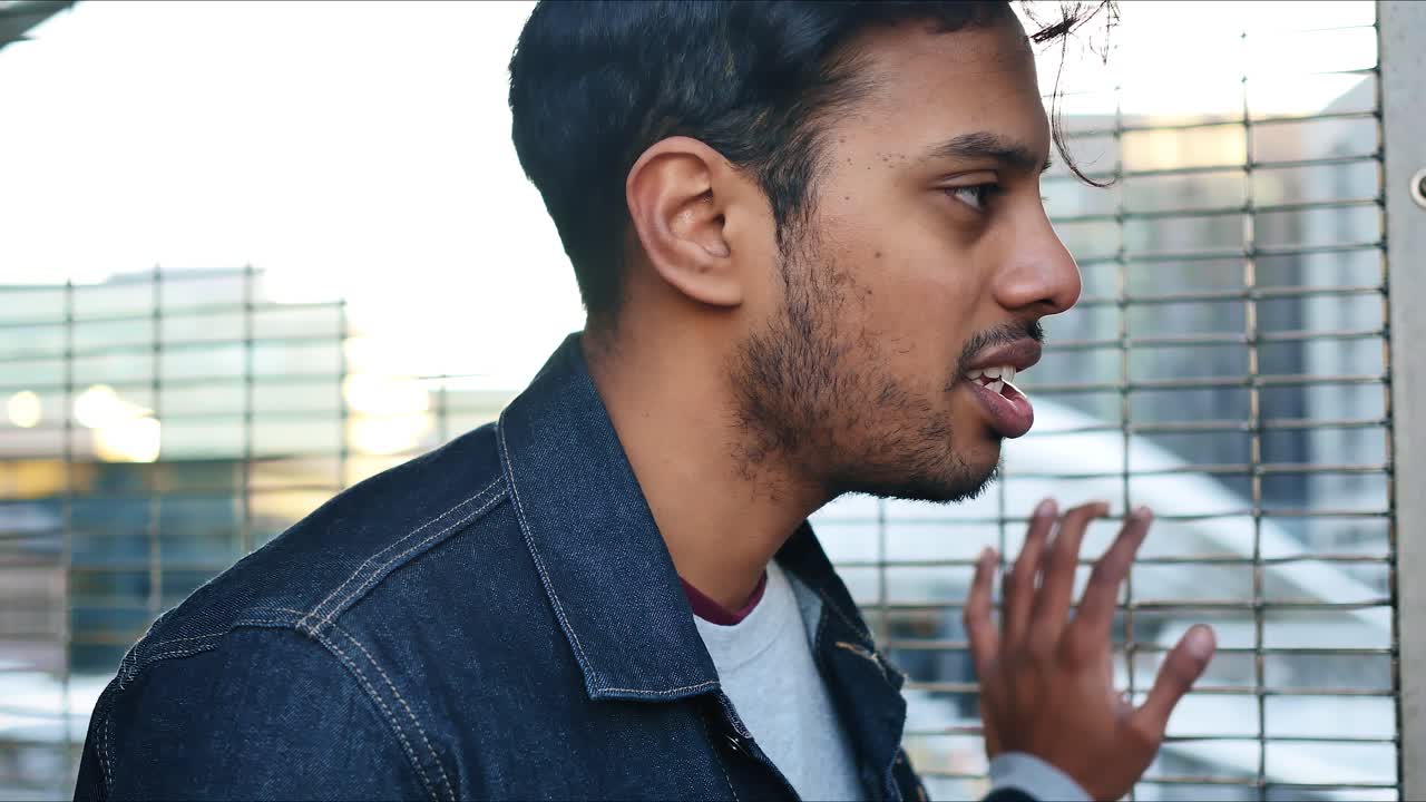 foto de perfil de un tipo con chaqueta de mezclilla agarrado a la cerca en una estación de tren que tiene una conversación seria con alguien fuera de marco
