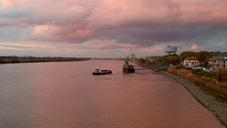 drone captures the pink light reflecting off a river as a boat turns from the dock