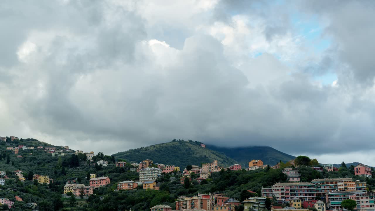 Clouds roll over a hillside town with colorful buildings and lush green landscape