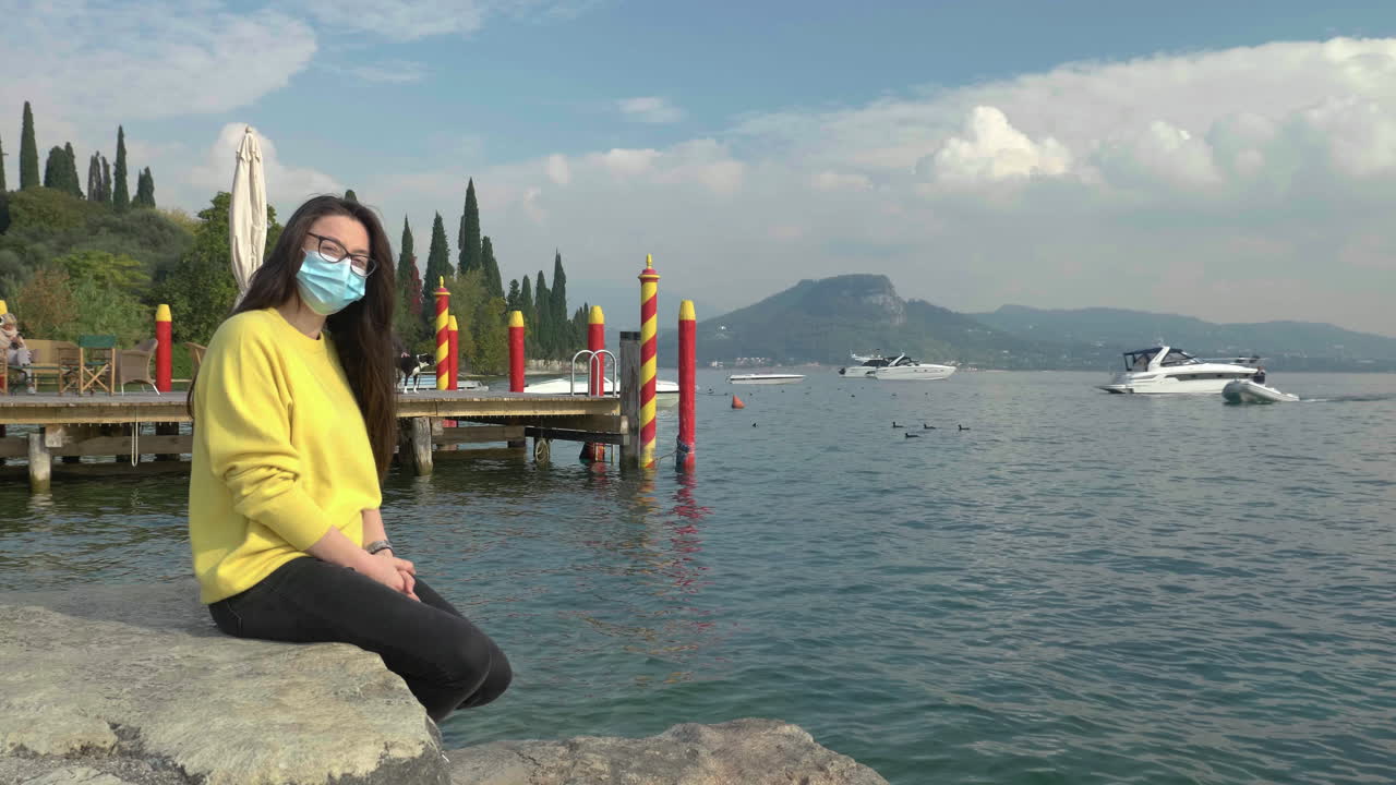 mujer joven con suéter amarillo brillante y cubierta facial disfrutando de un paisaje hermoso, relajante y escénico