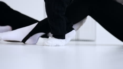 little feet of a baby in white socks and black pants step by the floor. legs of parents are at backdrop.