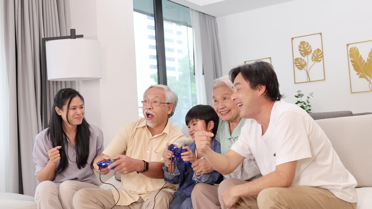 明るく居心地の良いリビングルームでビデオゲームを楽しむ、幸せな多世代のアジア系家族。