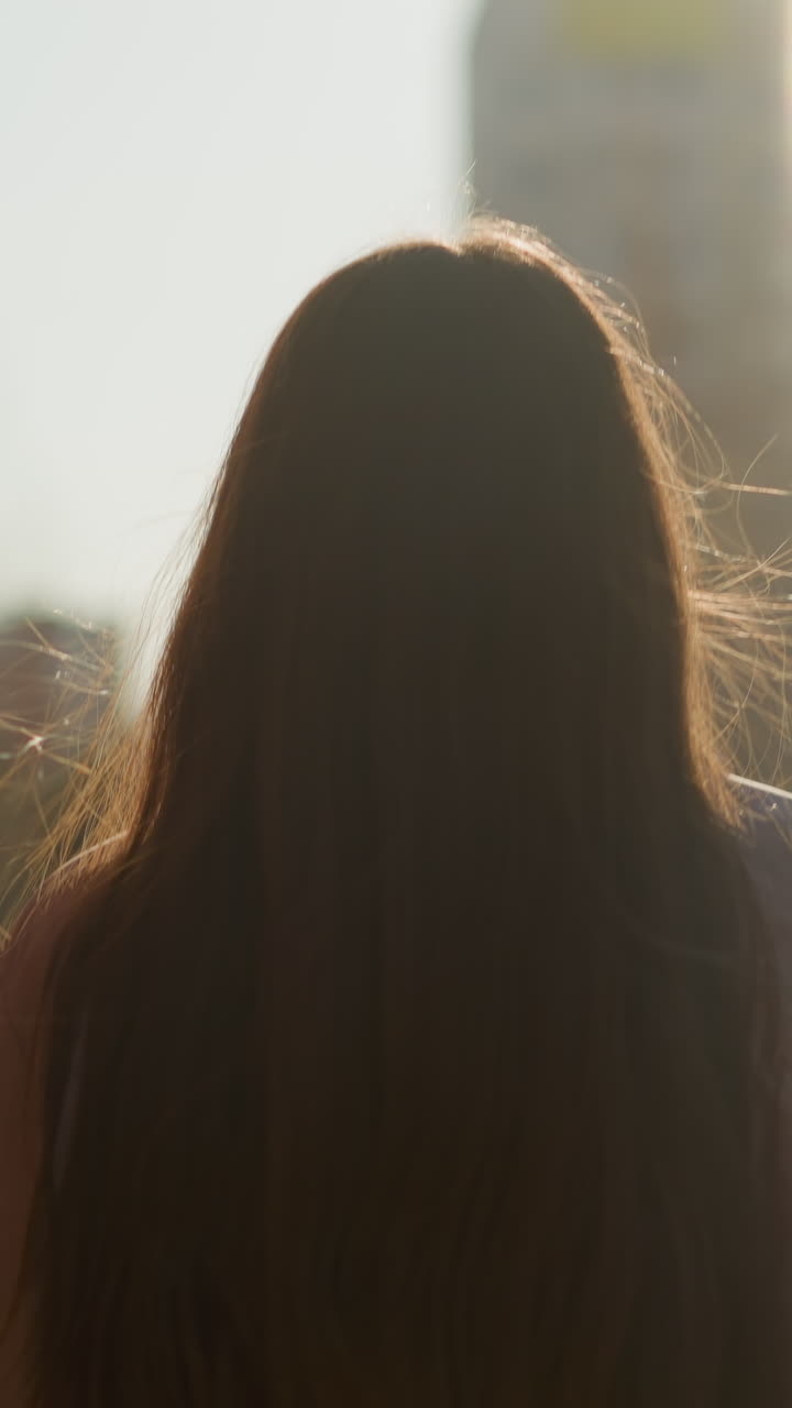 긴 갈색 머리카락이 흐르는 소녀의 클로즈업, 복아 재을 입고 스케이트보드를 들고 해가 지는 도시 지역을 걸어가며, 빛은 따뜻한 빛을 내며 조용한 분위기를 만니다.