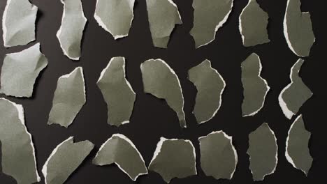 Video-of-close-up-of-multiple-torn-piece-of-green-paper-on-black-background