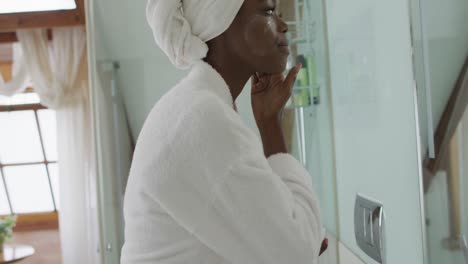 mujer afroamericana atractiva aplicando crema facial en el baño