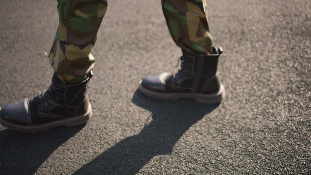 Black Soldier Toeing Forward In Military Boots On Sunlit Asphalt, Camouflage Pants And Textured Sole Visible, Focused Step Sequence, Gritty Detail Shot Capturing Rhythm And Endurance