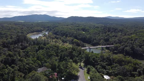 4k aerial drone shot of a tropical rainforest with a river and a bridge over it in north queensland, australia
