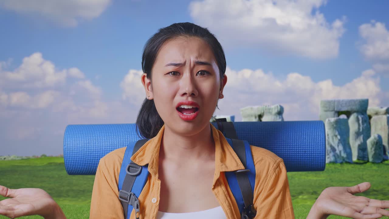 Close Up Of Puzzled Asian Female Hiker With Mountaineering Backpack Making Gestures Doubtfully And Saying Why While Traveling In Stonehenge