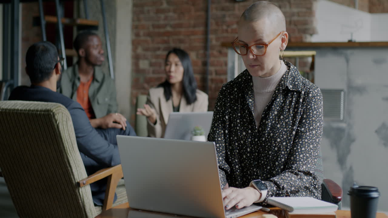 Businesswoman working on a laptop in a coffee shop with diverse colleagues