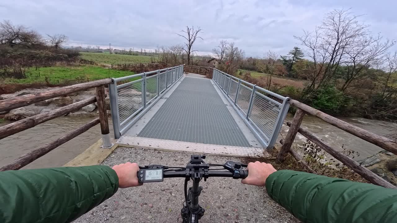 Vista en primera persona de un paseo en bicicleta eléctrica por un puente en un carril bici junto al río Molgora, cerca de Vimercate, Italia