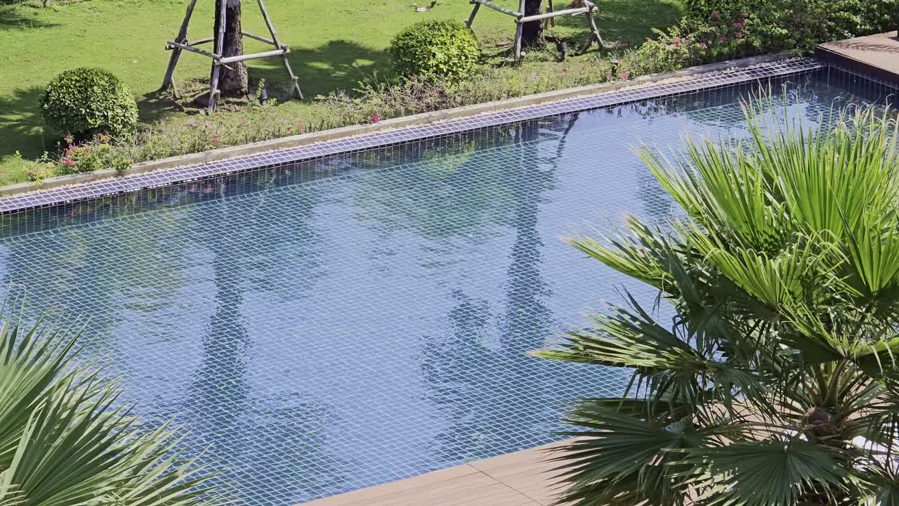Blå swimmingpool omgivet af frodigt grønt på hotel i Thailand.